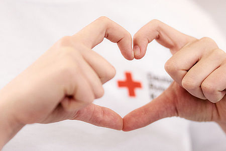 Save the Date Zwei Hände formen ein Herz, im Hintergrund ist ein Rotes-Kreuz-Logo